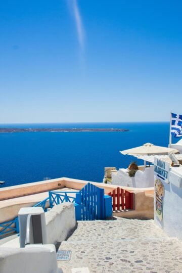 Santorini seaside view with blue gates and Greek flag on a sunny day – best time to visit Greece for summer island travel