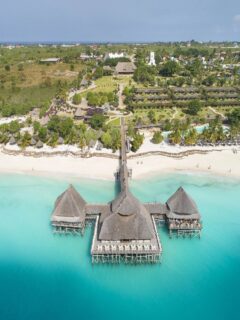 Blue Safaris resort view in Zanzibar featuring an overwater restaurant, white sand beach, and turquoise ocean.