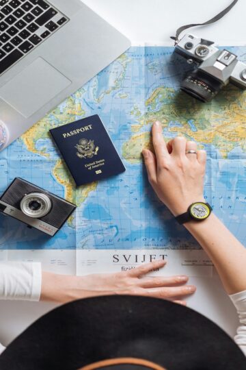 Person planning international travel using a world map, passport, laptop, and camera, researching destinations and travel insurance options for global trips in 2026